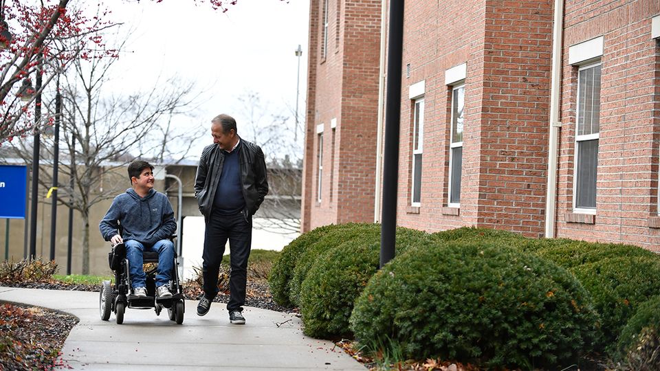 A person in a wheelchair strolling alongside someone else on the campus